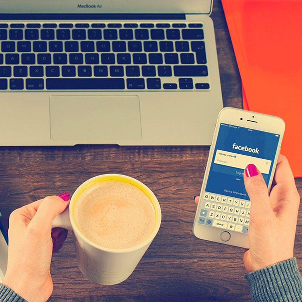 A woman logs into Facebook on her phone while enjoying coffee